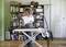 A woman is ironing clothes in a cosy living room with books in the background.