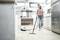 A woman is vacuuming the floor in a modern kitchen using a cordless handheld vacuum cleaner.