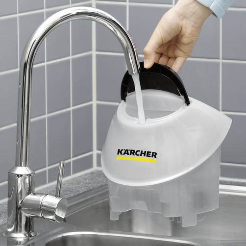 A hand is holding a Kärcher water tank under a tap to fill it. The tap is located in a kitchen in front of blue tiles.