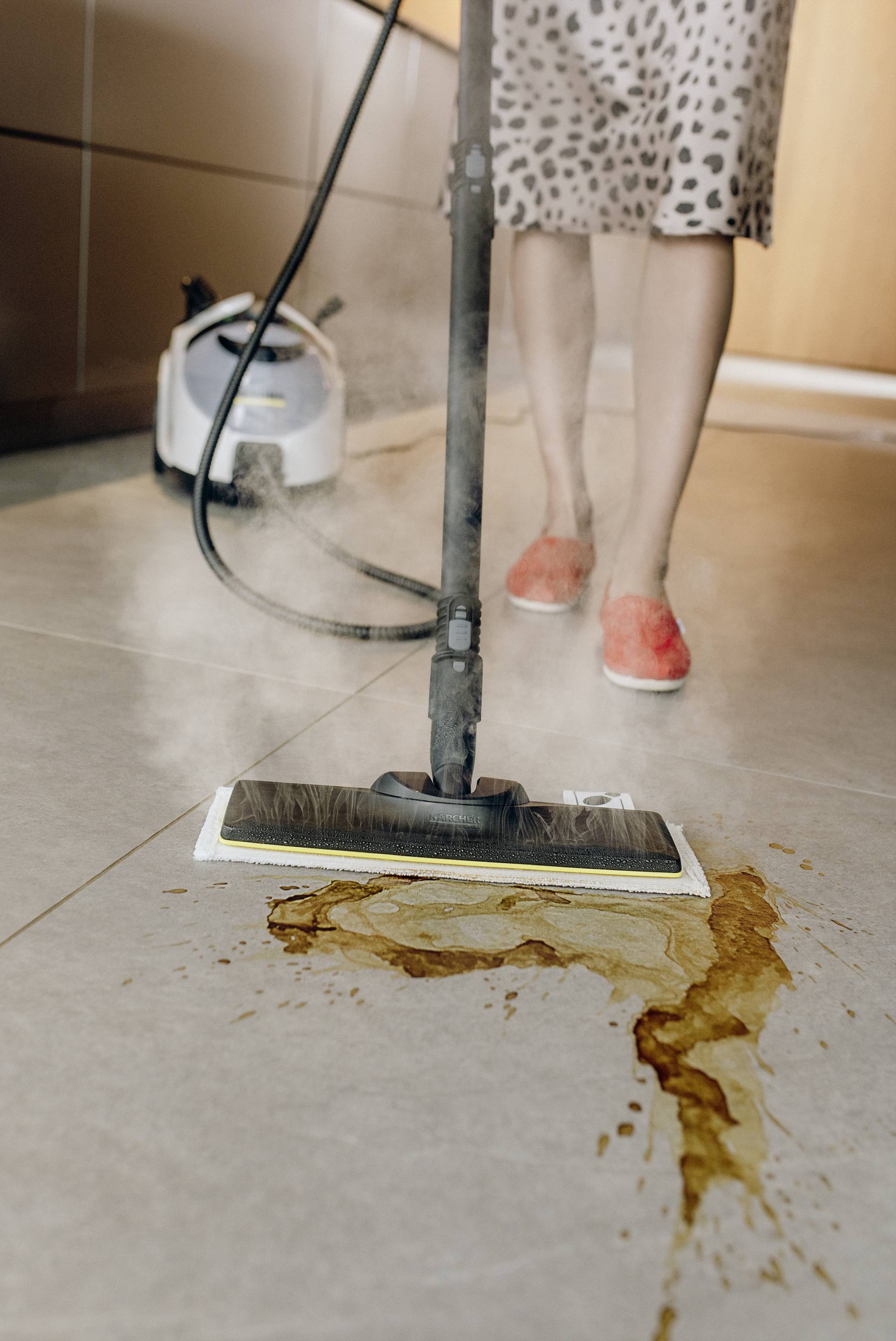 A person is cleaning a floor with a steam cleaner. A spilled liquid is being cleaned up from the floor.