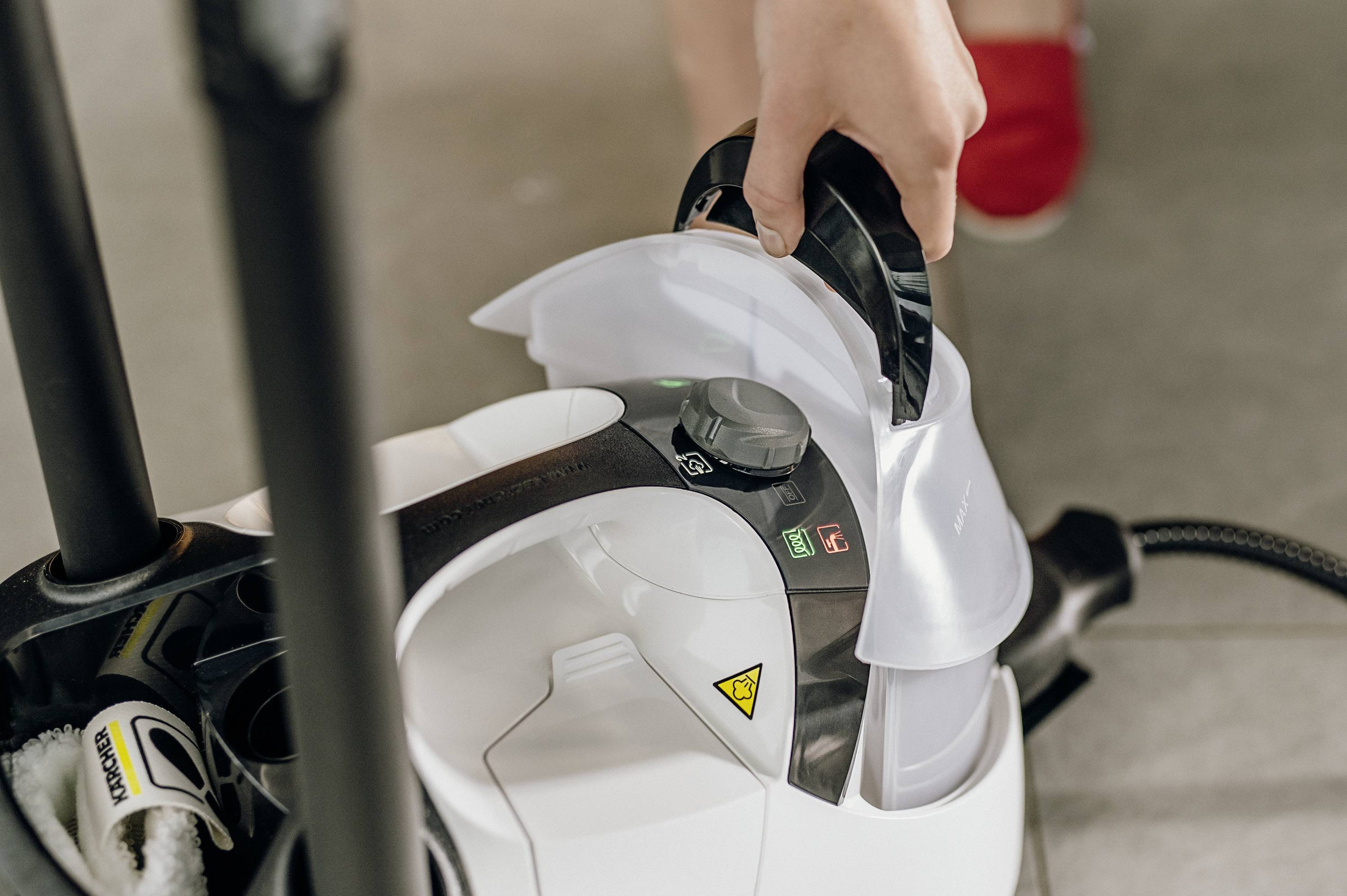 A person opens the water tank of a steam cleaner to fill it. The cleaner has black and white elements.