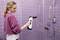 A person is cleaning a glass shower screen with an electric window cleaner in a lavender-coloured bathroom.