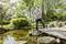 A man stands on a jetty by a pond, testing the water quality with a measuring device. In the background: lush vegetation.