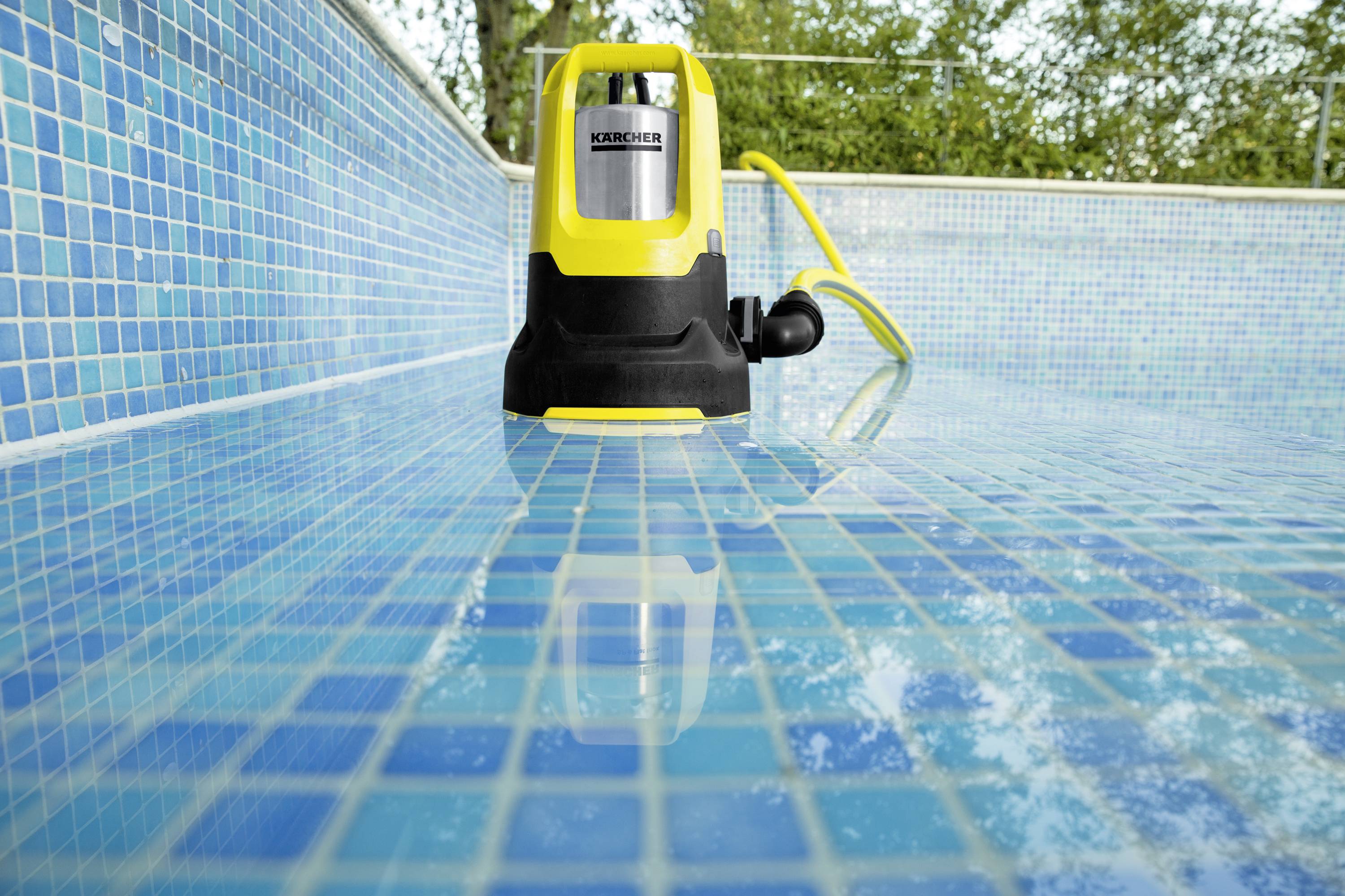 A yellow water pump stands in a partially filled pool. The tiles are blue. The pump is connected to a yellow hose.