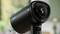 Black hairdryer with digital display '5'. It is standing on a table, surrounded by a blurred green environment in the background.