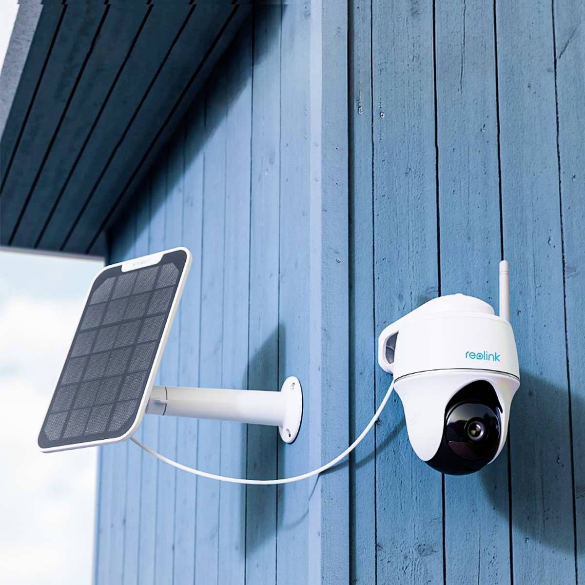 Security camera mounted on a blue wall, connected to a solar panel for power supply.