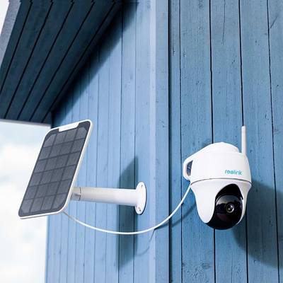 Security camera mounted on a blue wall, connected to a solar panel for power supply.