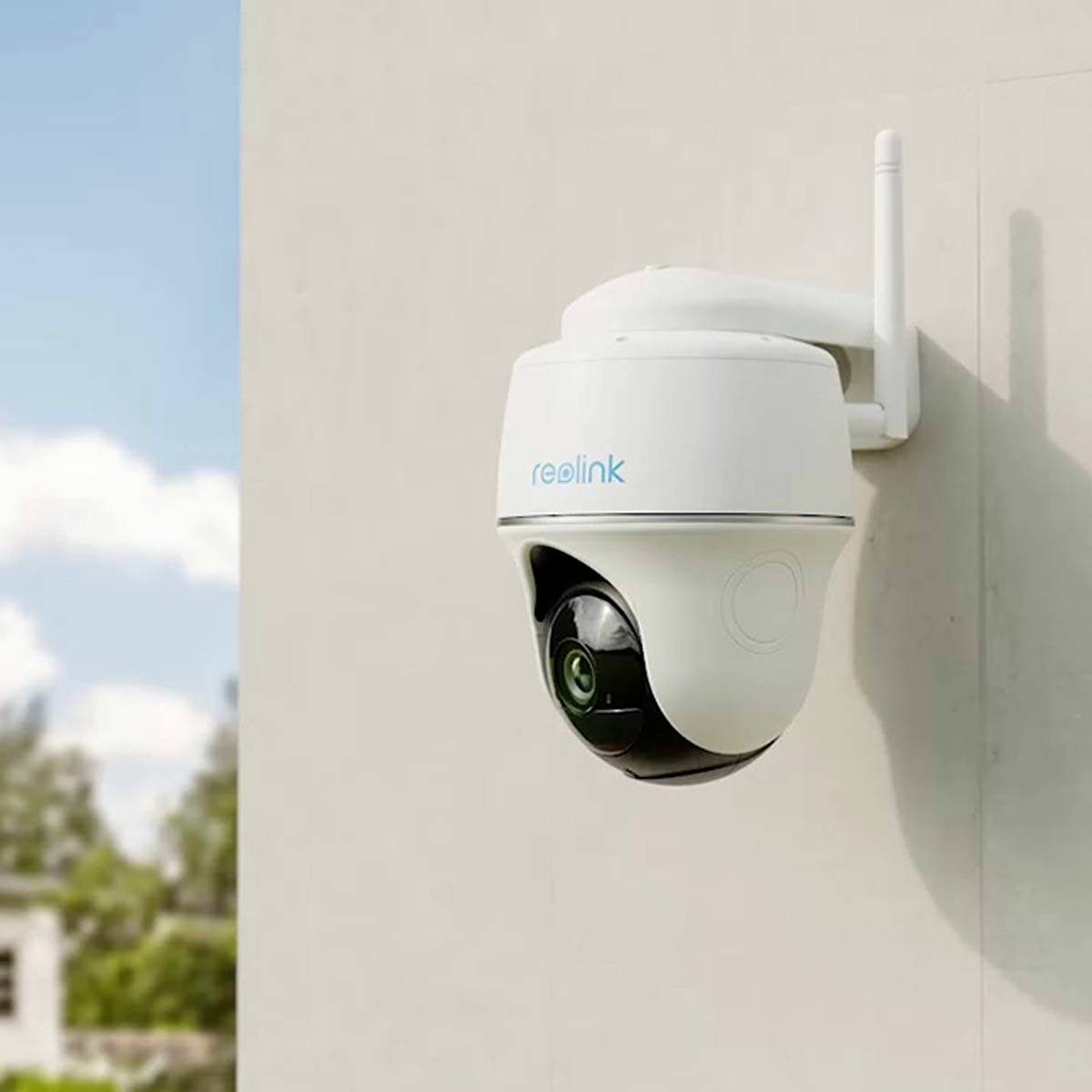 Security camera mounted on an exterior wall, with blue sky and trees in the background, capturing surveillance images.