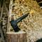 An axe is stuck in a tree stump. In the background, a stack of chopped firewood can be seen.