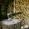 An axe is stuck in a tree stump in front of a pile of chopped firewood inside a wooden cabin.