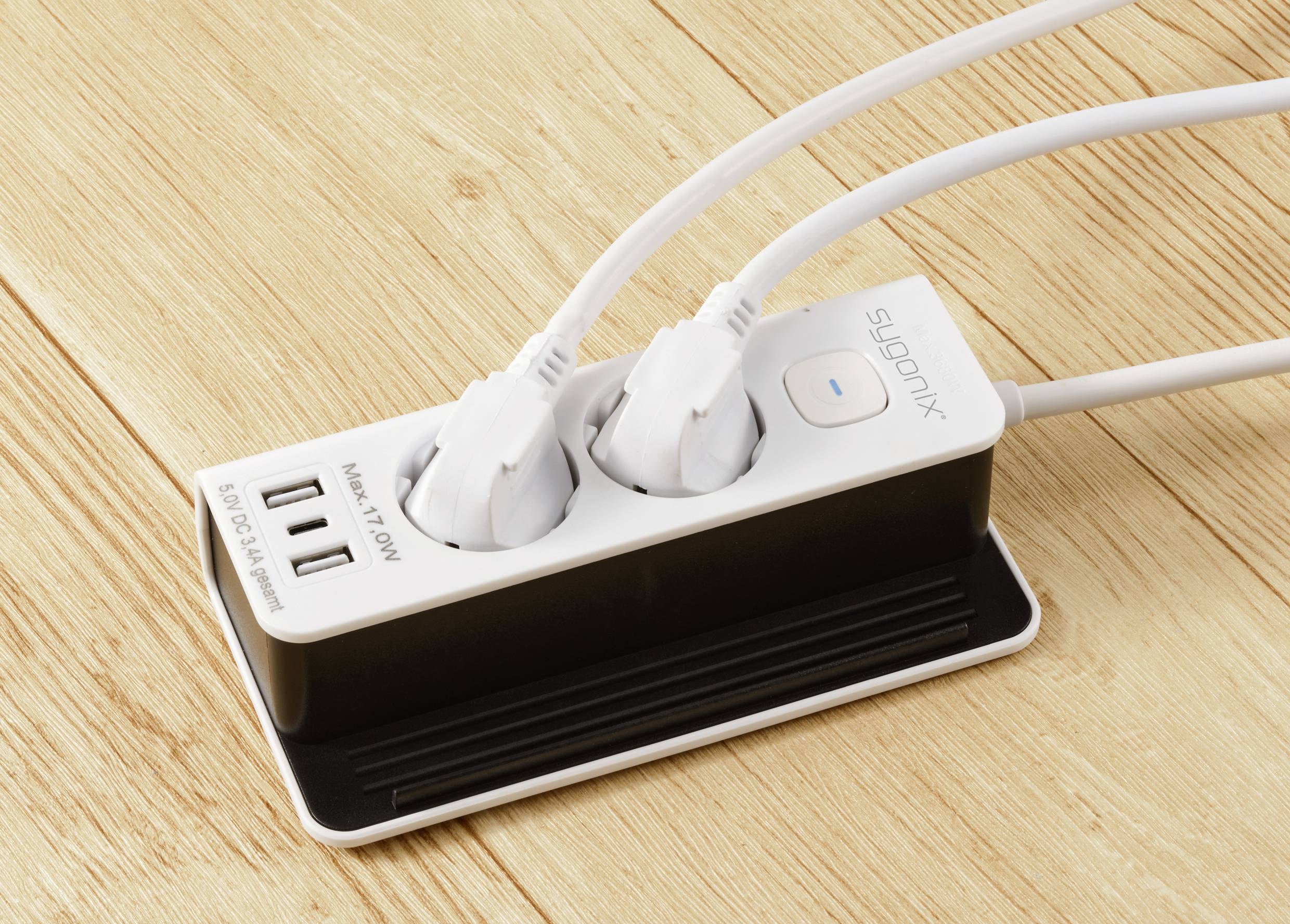 Two white plugs are inserted into a power strip lying on a wooden surface. The strip has two USB ports.