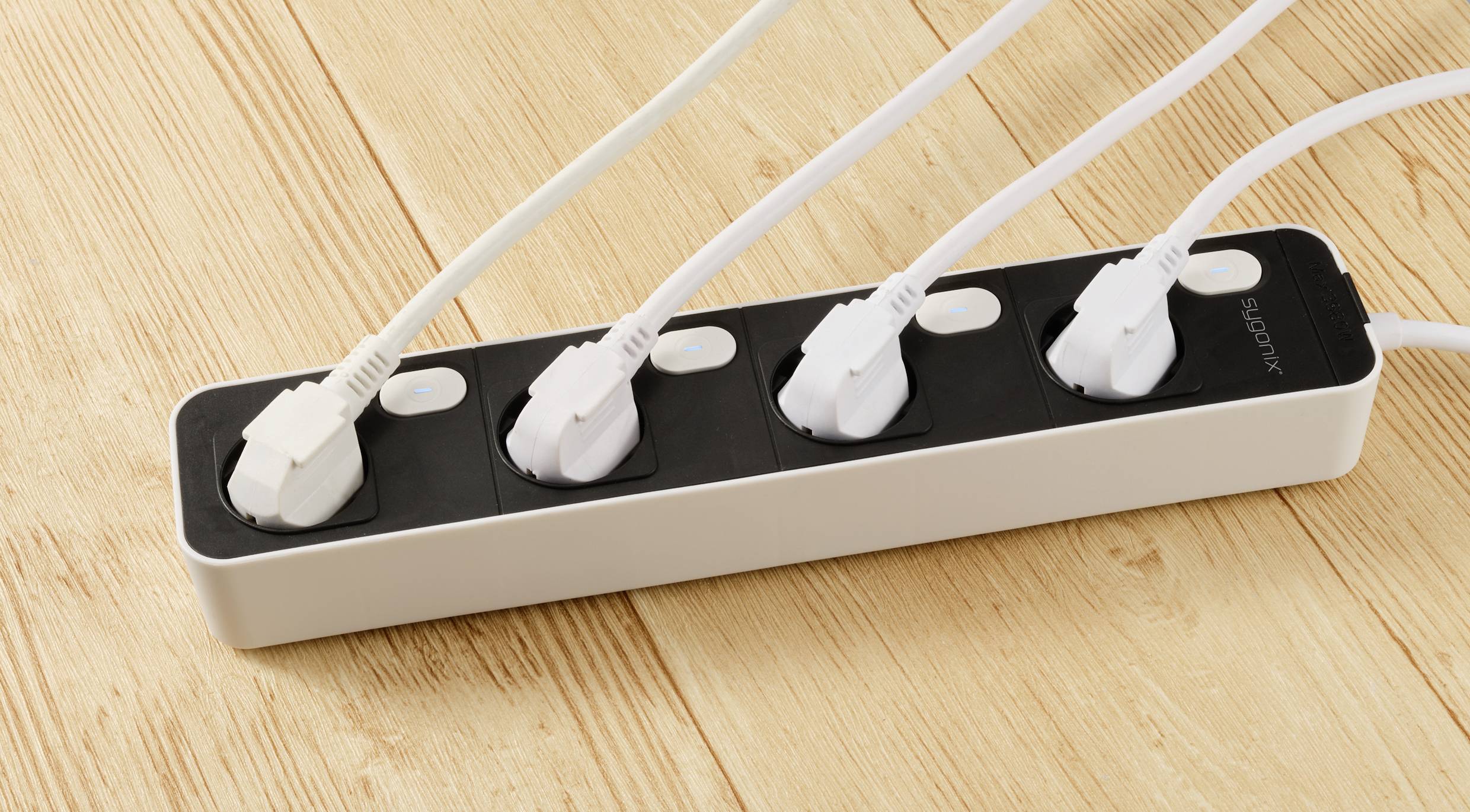 Four-way power strip with four white cables plugged in, resting on a wooden floor.