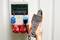 A person is holding a measuring device close to an electrical control cabinet with red and blue electrical connectors. The device is displaying measurement readings.