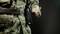 A person in camouflage uniform draws a pen from a holder on their belt. The background is dark, with the focus on the action.
