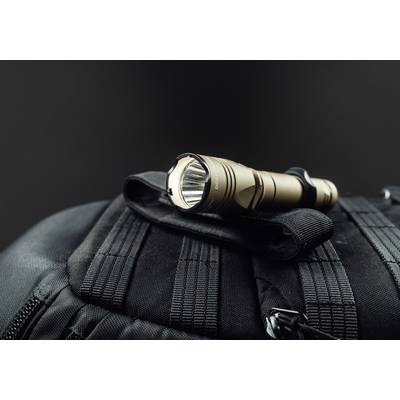 Torch lies on a black rucksack. The lamp is switched on and emitting light. The background is dark.