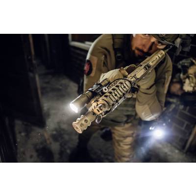 A soldier in tactical gear aims a weapon in a dimly lit room. The torch mounted on the weapon illuminates the way.