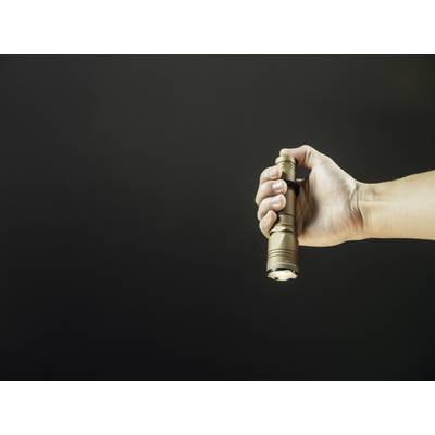 A hand holds a switched-on torch against a dark background. The torch is shining light forwards.