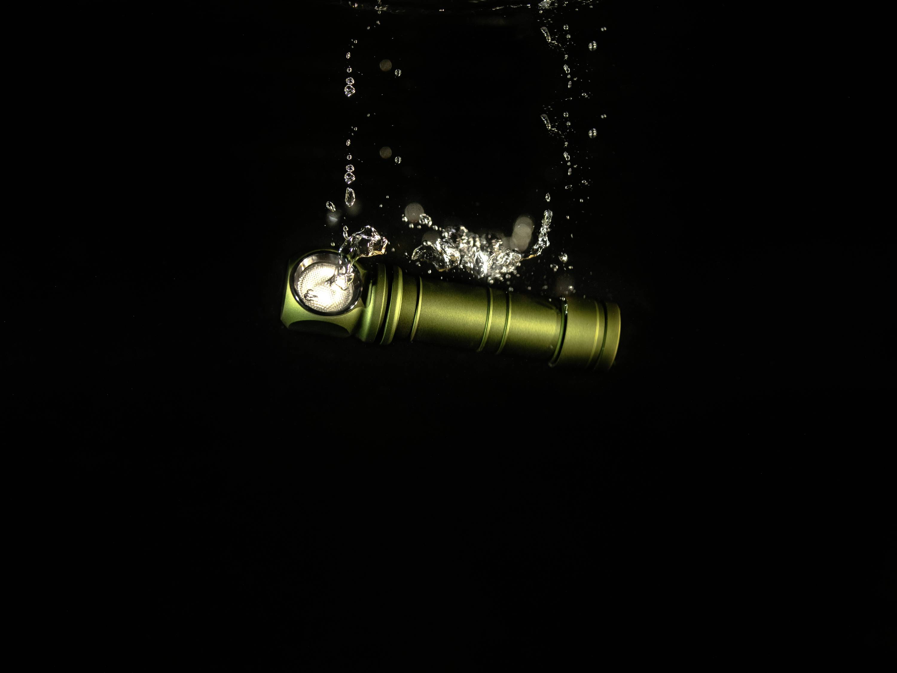 A green torch falls into water, bubbles rising. A dark background highlights the movement and brightness.