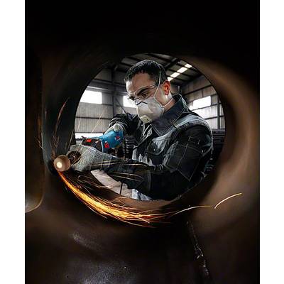 A person is wearing protective clothing and grinding metal with an electric tool. Sparks are flying while working in a workshop.