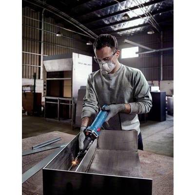 A man is wearing protective clothing and welding a piece of metal in a workshop. He is using an electric welding machine.