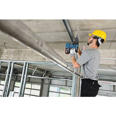 A construction worker wearing a hard hat and ear protection is using a drill to attach a metal strip to the ceiling of a building.