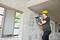A construction worker wearing a yellow hard hat is drilling into a concrete wall on a building site.