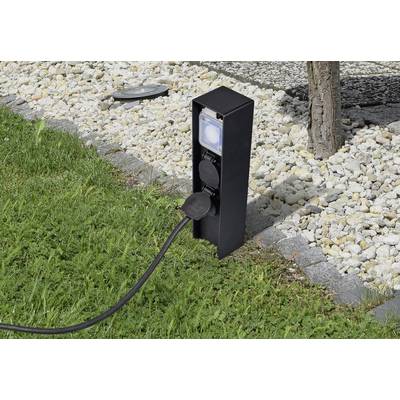 Black outdoor socket mounted on a tree in the garden, with a cable plugged in. Surrounded by grass and pebbles.