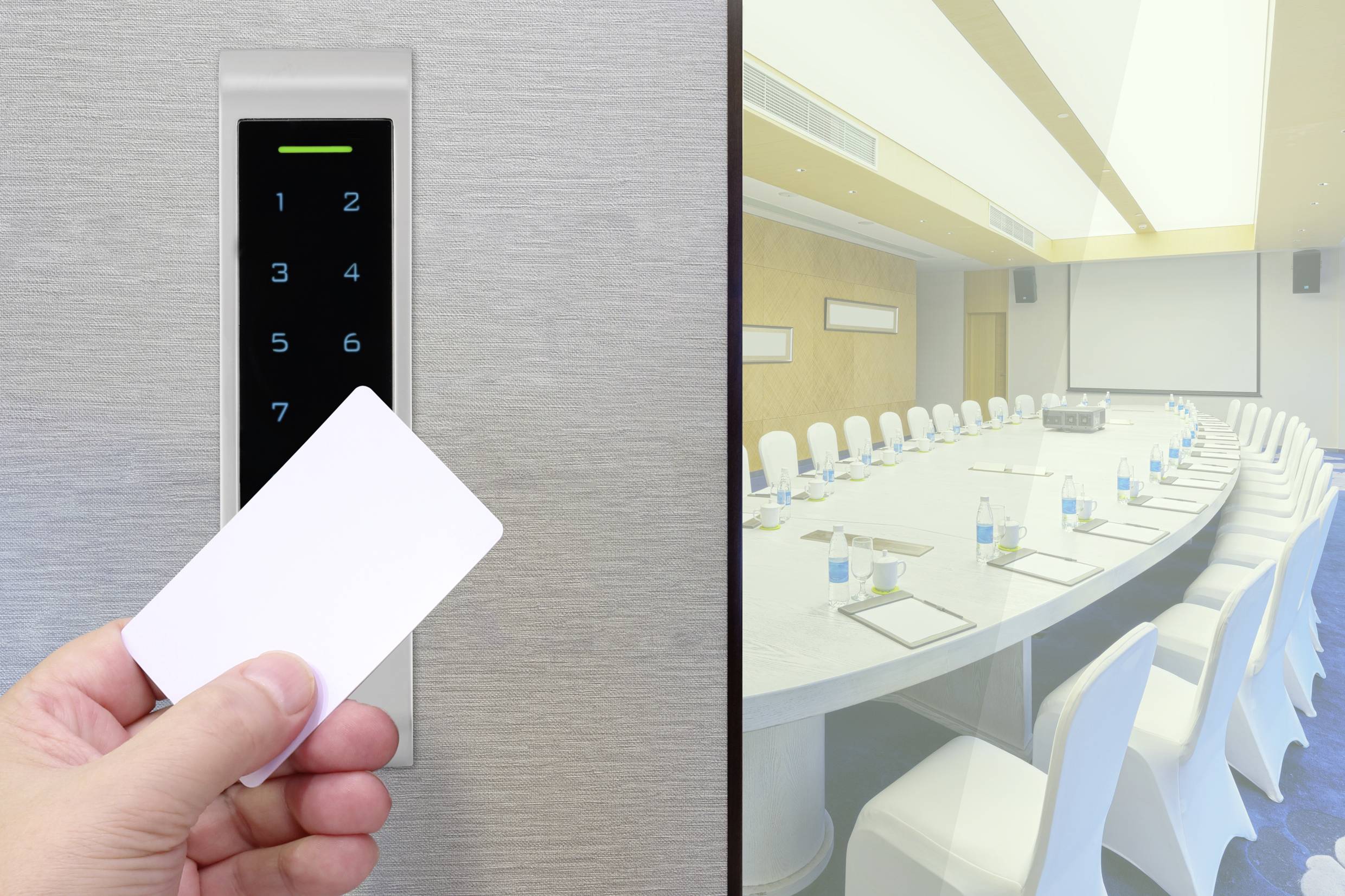 A hand holds an access card in front of an electronic lock. In the background, an empty conference room with a large table and chairs.