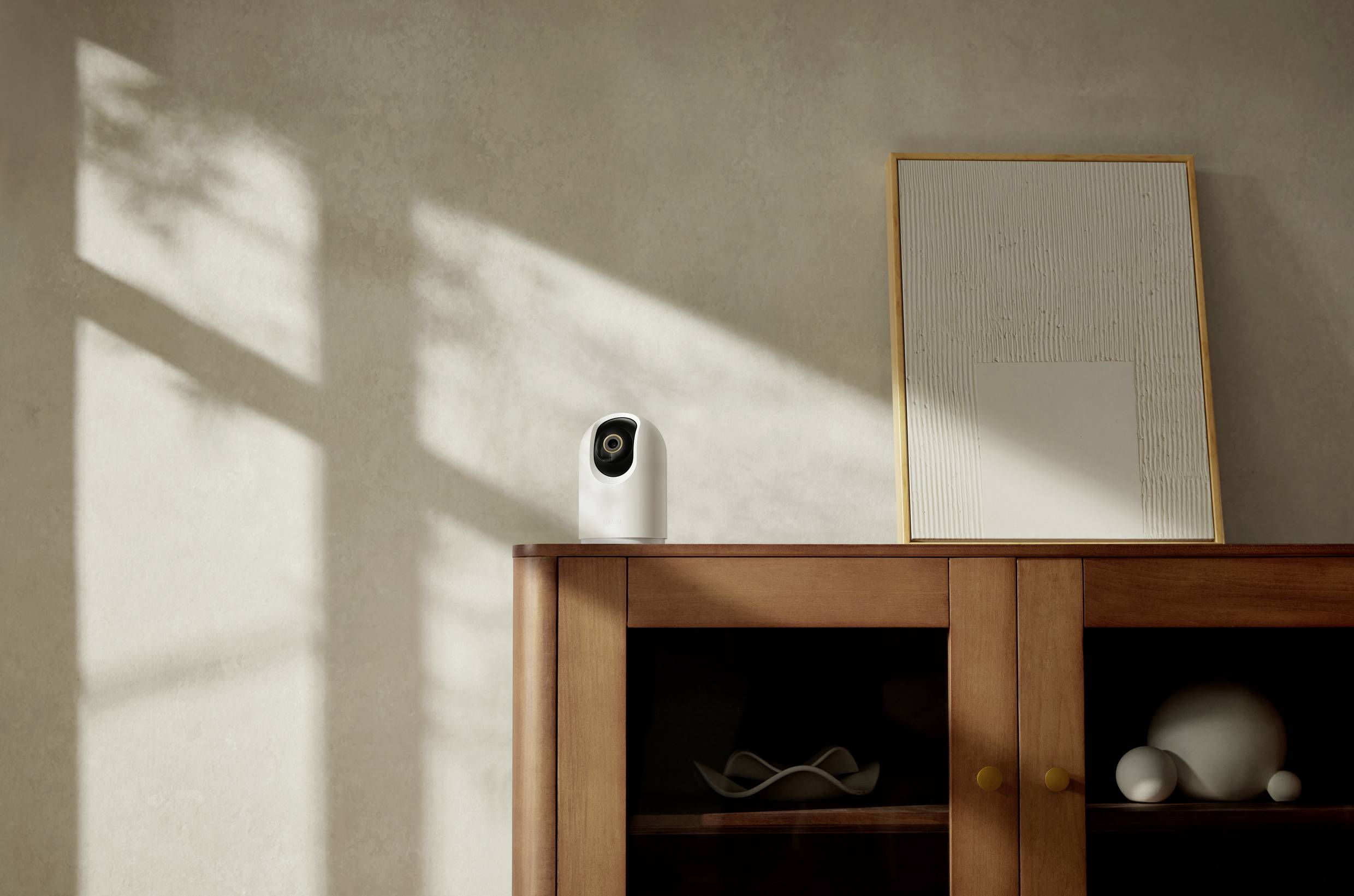A white camera on a wooden cabinet next to a picture frame, illuminated by sunlight streaming through a window.
