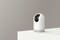 A white security camera stands on a white base against a grey background; modern, minimalist design.