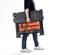 A person is carrying a black toolbox with an orange compartment. The person is wearing jeans and white trainers.