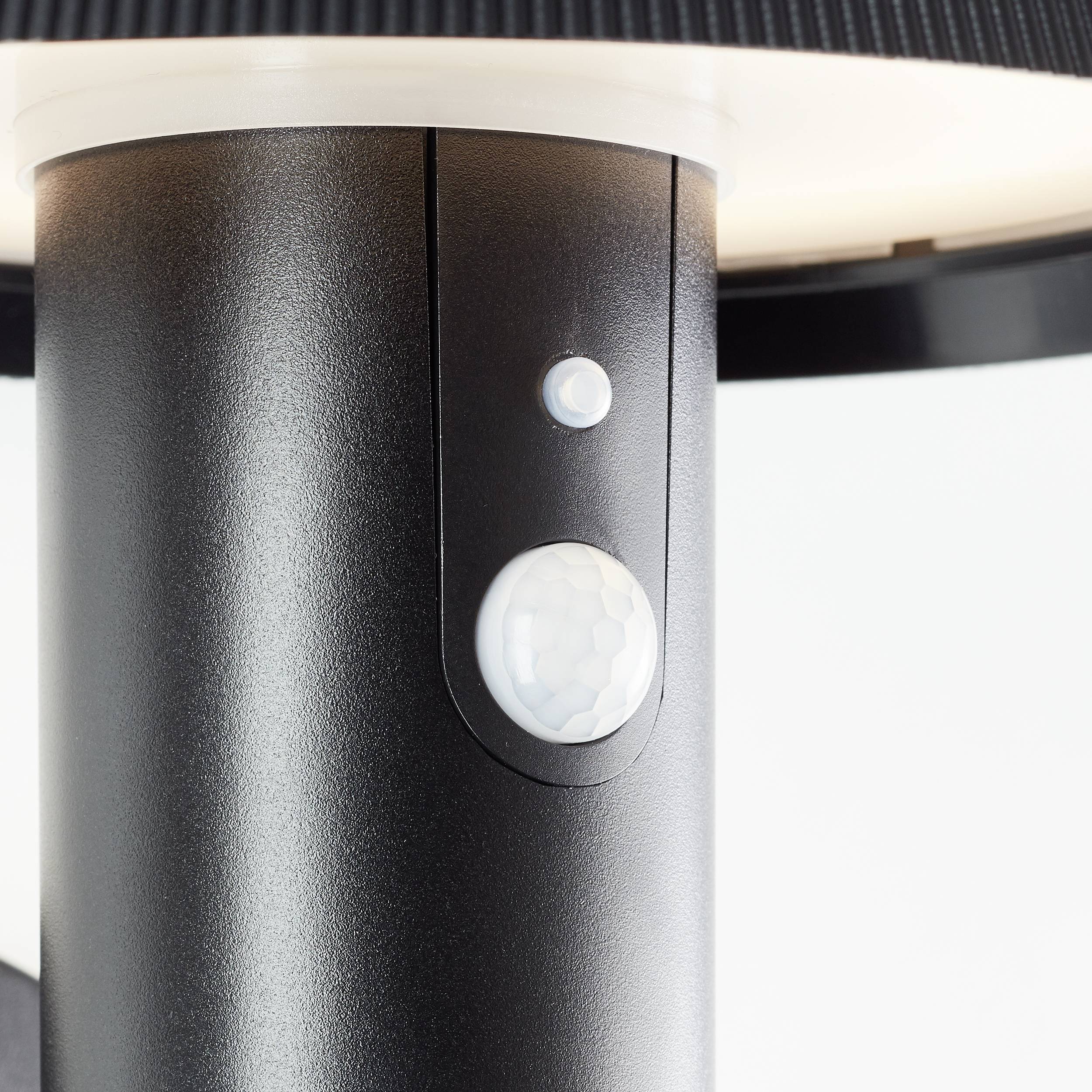 Close-up of a motion sensor on a black floor lamp, emitting a soft light.