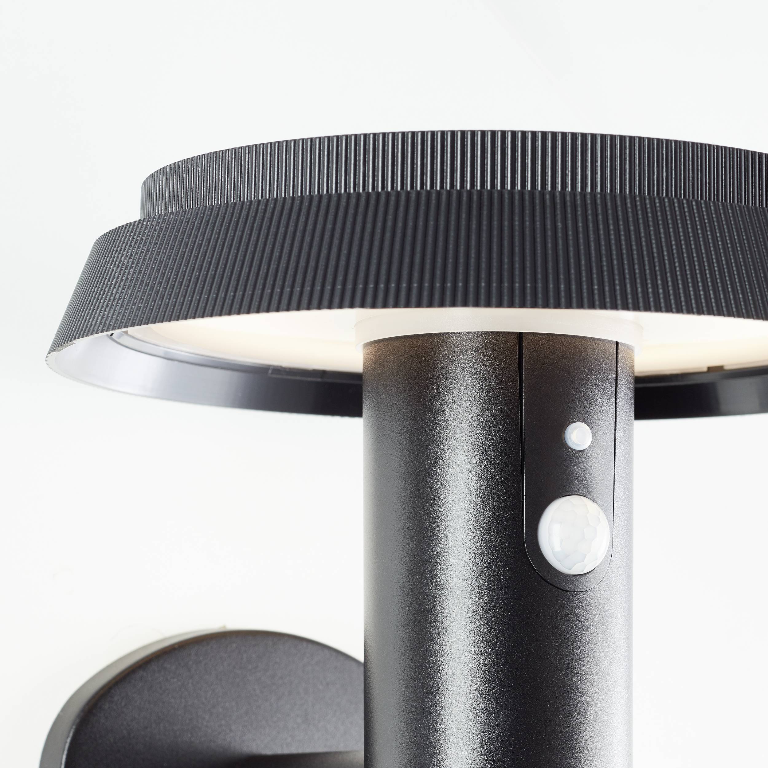 A black outdoor lamp with a motion sensor, mounted on a wall bracket.