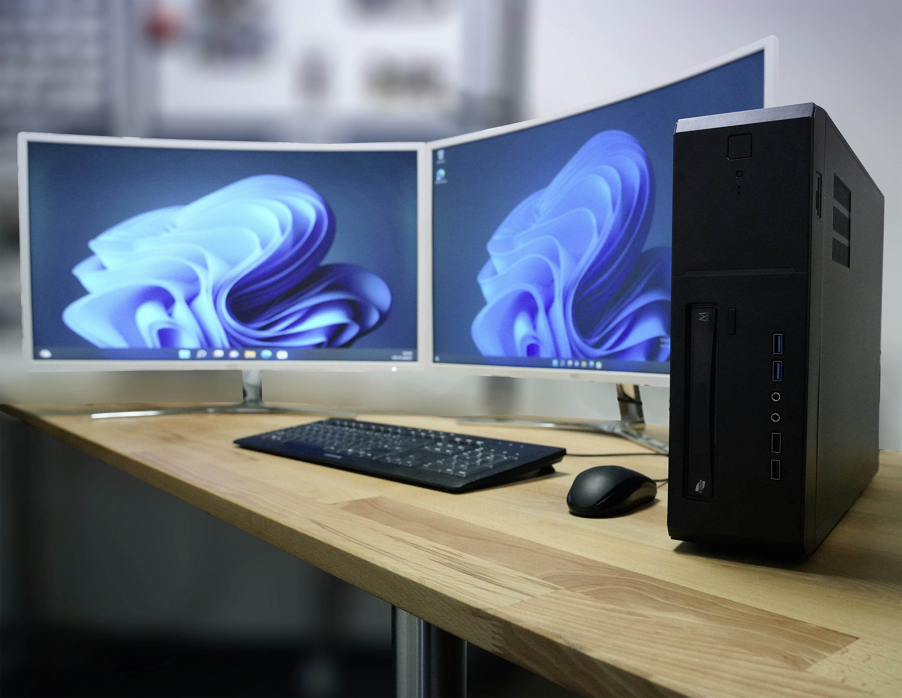 A computer workstation with two curved monitors, a black computer tower, a keyboard and a mouse on a wooden desk.