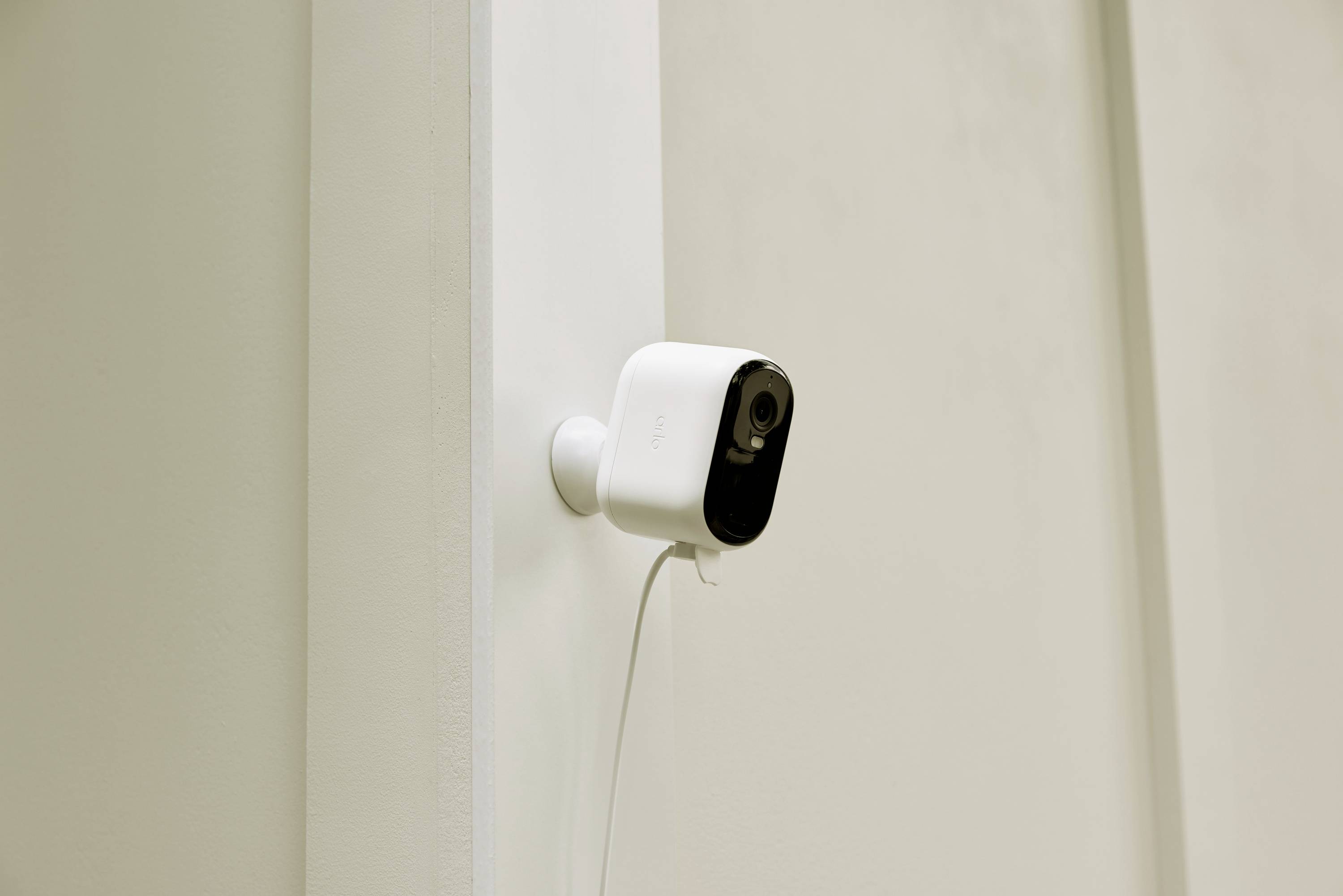 White surveillance camera mounted on a wall. Cable runs down from the camera.