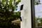 A solar-powered security camera is mounted on a house wall, surrounded by green trees in the background.