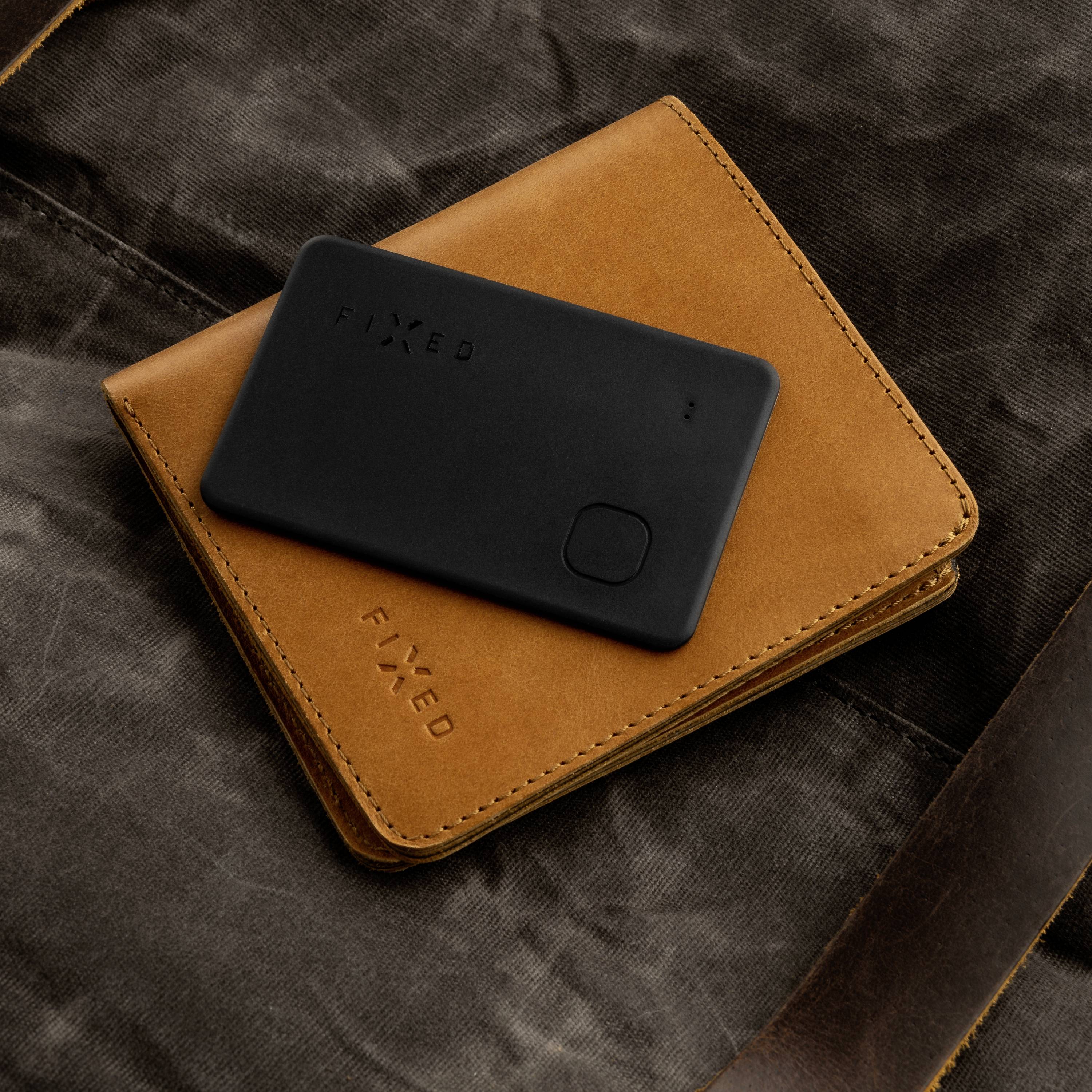 A black card holder rests on a brown leather wallet with the embossed text 'FIXED', both placed on a dark fabric background.