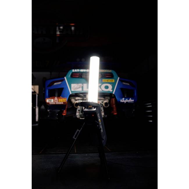A racing car is situated in a workshop, illuminated by a bright light in the foreground. The car is partially obscured.