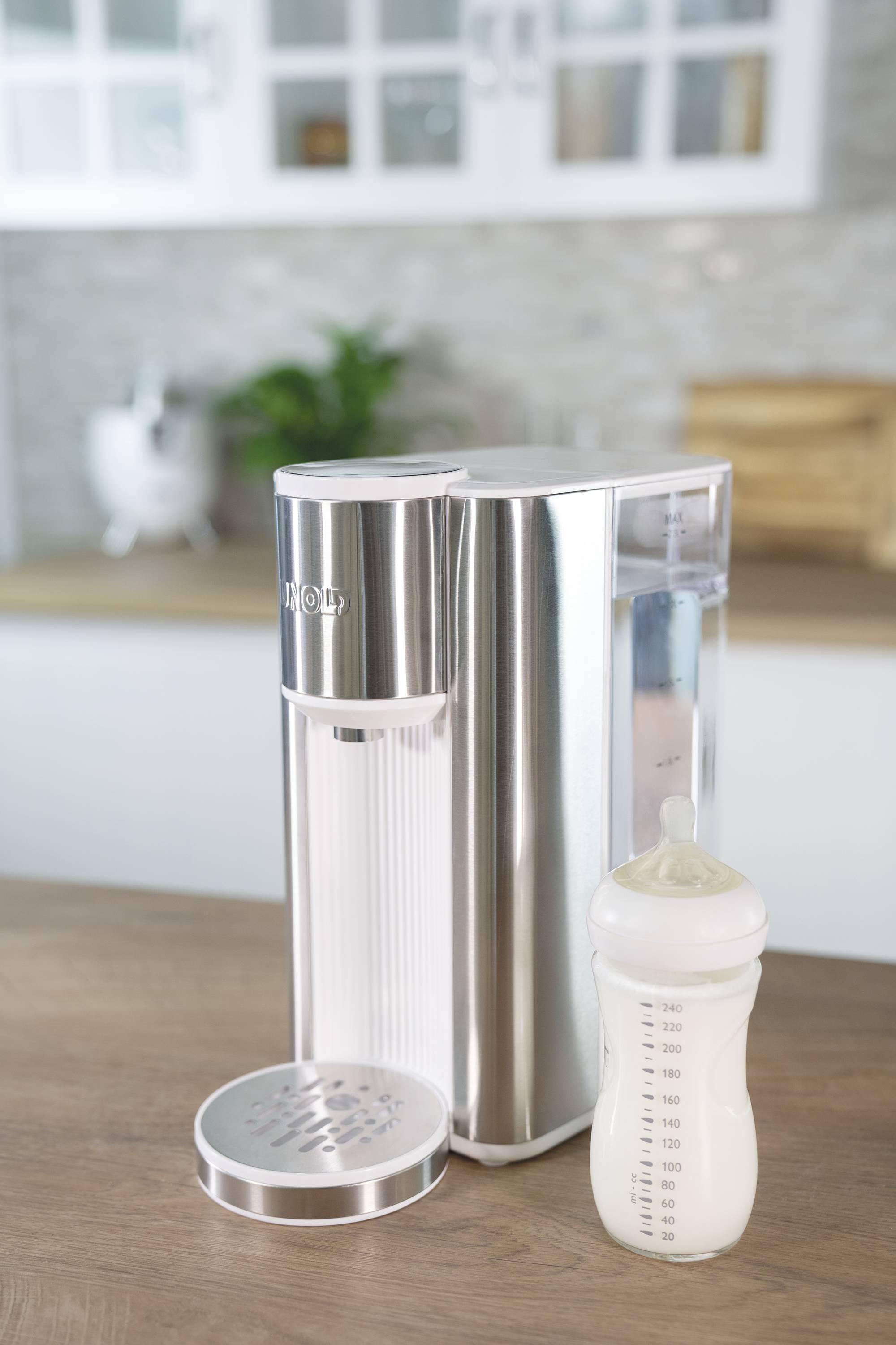 Breast pump on a kitchen worktop next to a baby bottle filled with milk, with blurry kitchen elements in the background.
