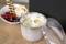 Ice cream in a metal bowl with a lid on a wooden surface; cookies and fruits in a white bowl are in the background.
