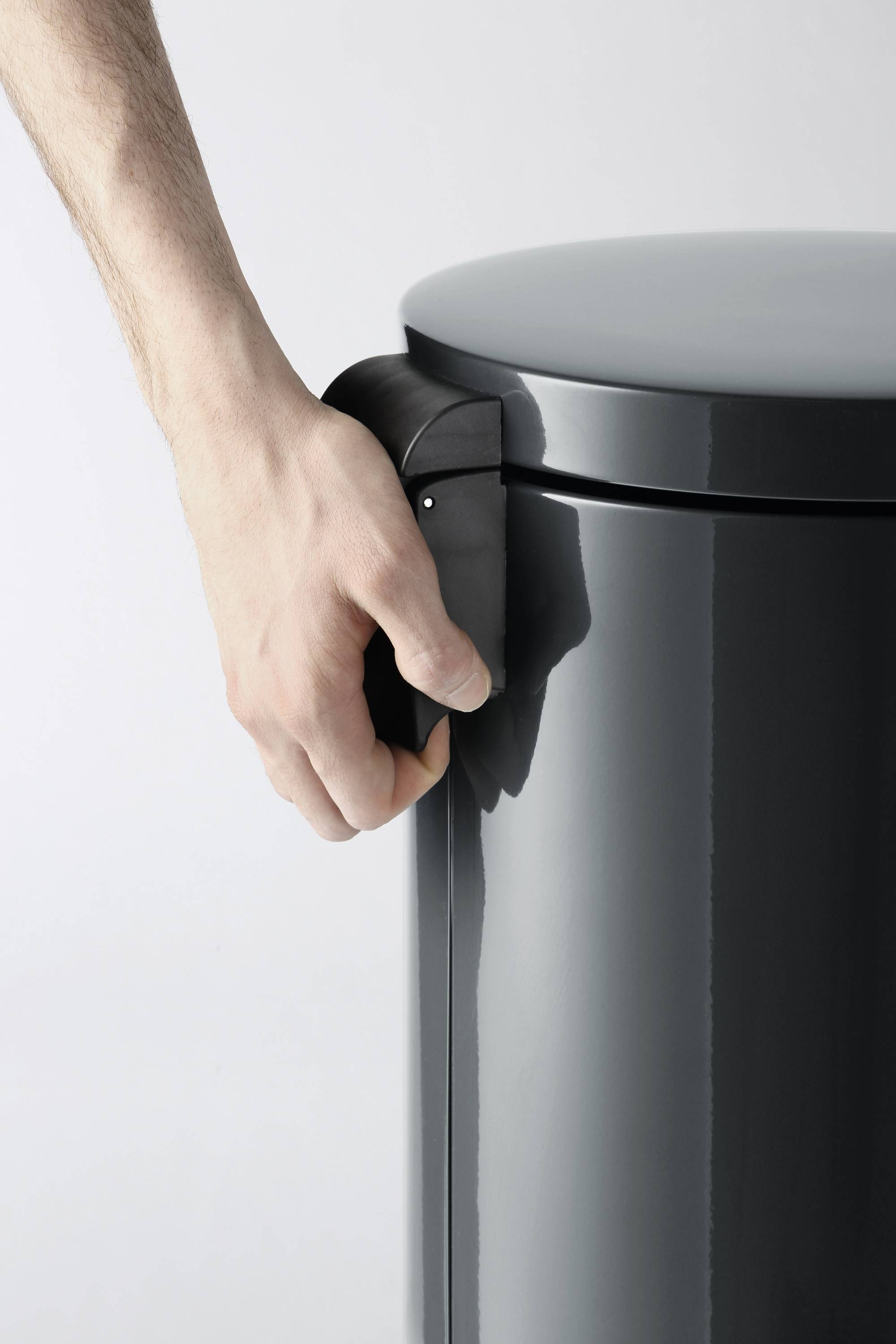 A hand opens a round, dark grey rubbish bin.