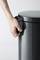A hand opens a round, dark grey rubbish bin.