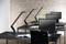 Black desks in an open-plan office with monitors and desk lamps, in front of a brick wall. An open book lies on a table.