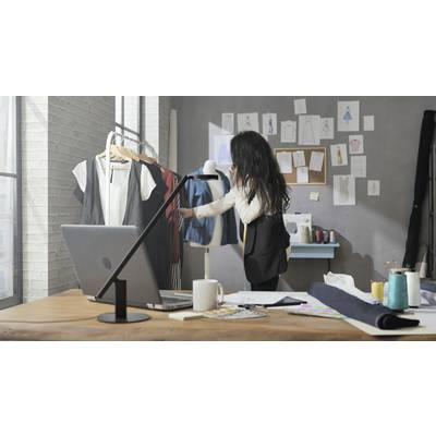 A designer is on the phone in a fashion studio. She is examining garments on a stand. Sketches can be seen in the background.