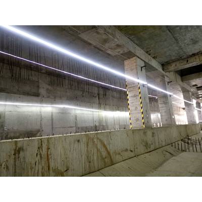 A concrete structure in a tunnel or underground space with visible steel reinforcement bars and linear lighting along the ceiling.