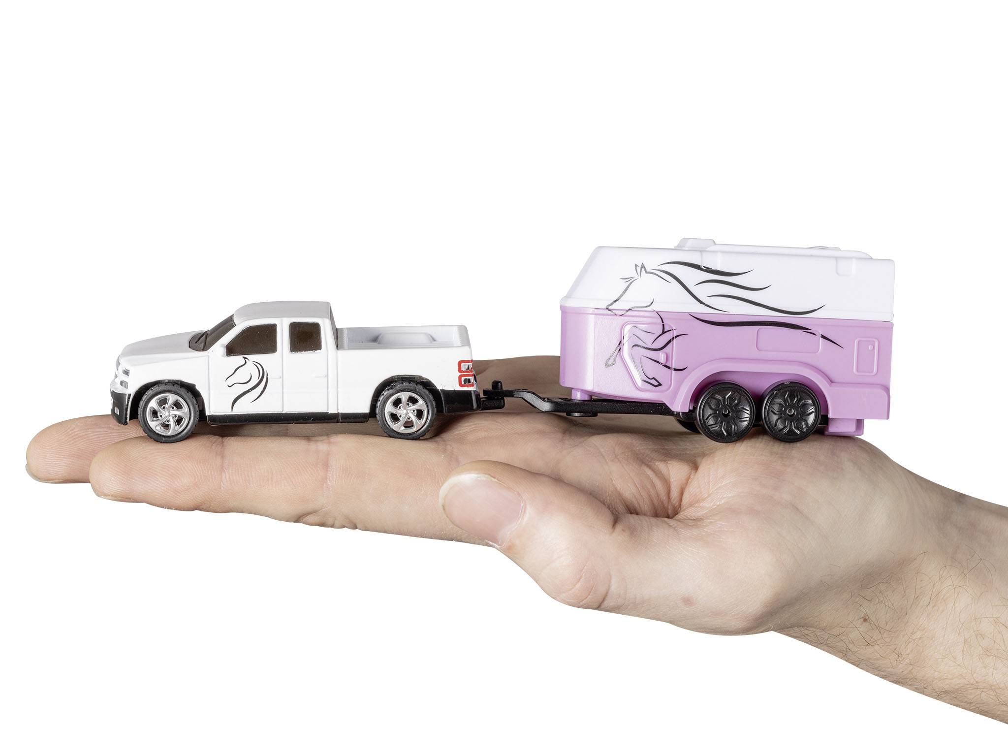 A hand is holding a small toy car with a trailer. The car is white, the trailer is pink, both decorated with horse illustrations.