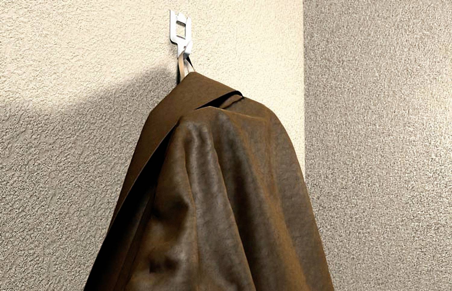 A brown jacket is hanging on a hook on the wall. The wall has a textured surface.