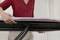A person in a red blouse is setting up an ironing board. The focus is on the hands adjusting the board.