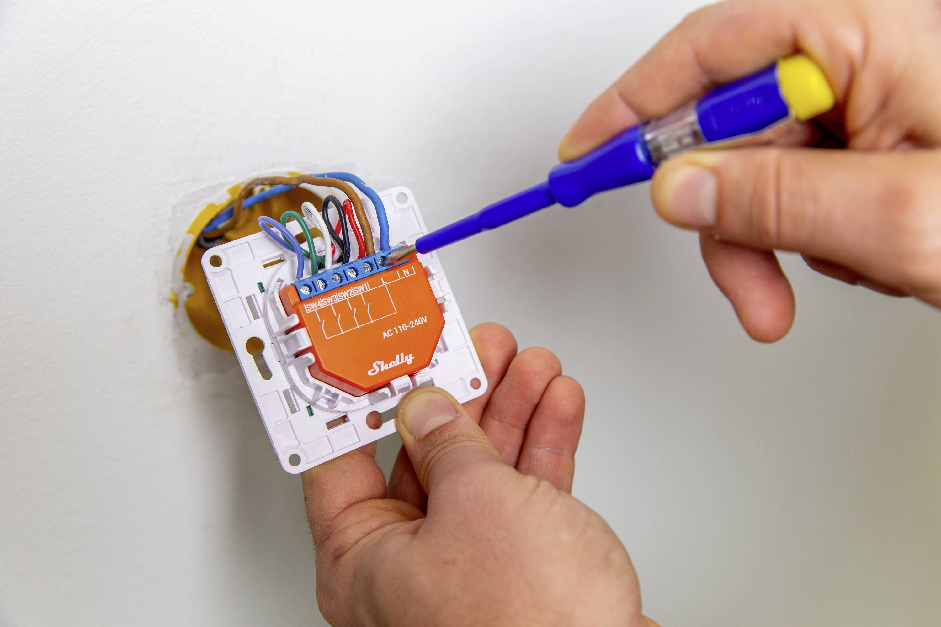 A person is installing an electrical switch with a screwdriver. Several cables are connected.