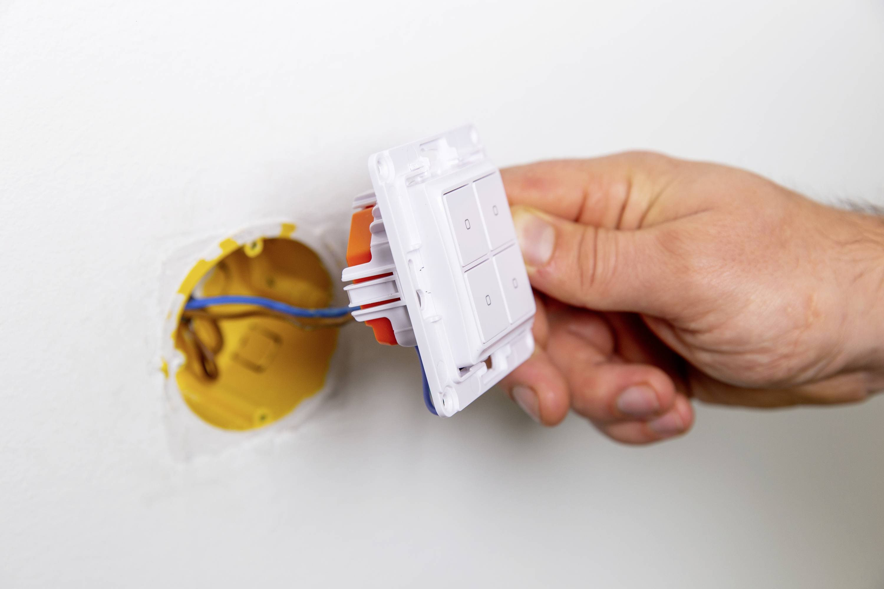 A hand is installing or removing a light switch from a wall opening. Electrical wires are visible.